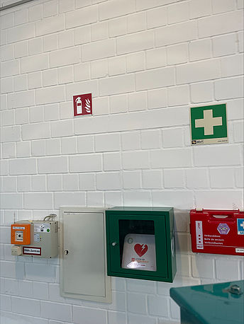 Durch den Haupteingang geradeaus, AED im Wandkasten an der Wand gegenüber